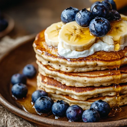 A plate of banana cottage cheese pancakes with Greek yogurt, berries, and honey drizzle.